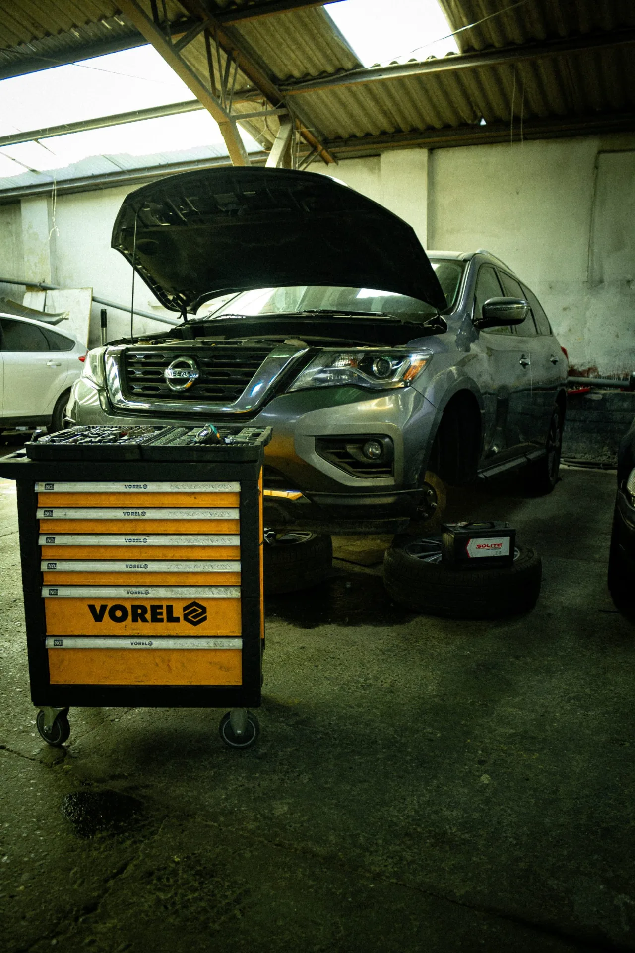 SUV con capó abierto junto a un carro de herramientas amarillo
